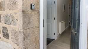 A stone wall with a security device, a white door, and a hallway with a radiator.