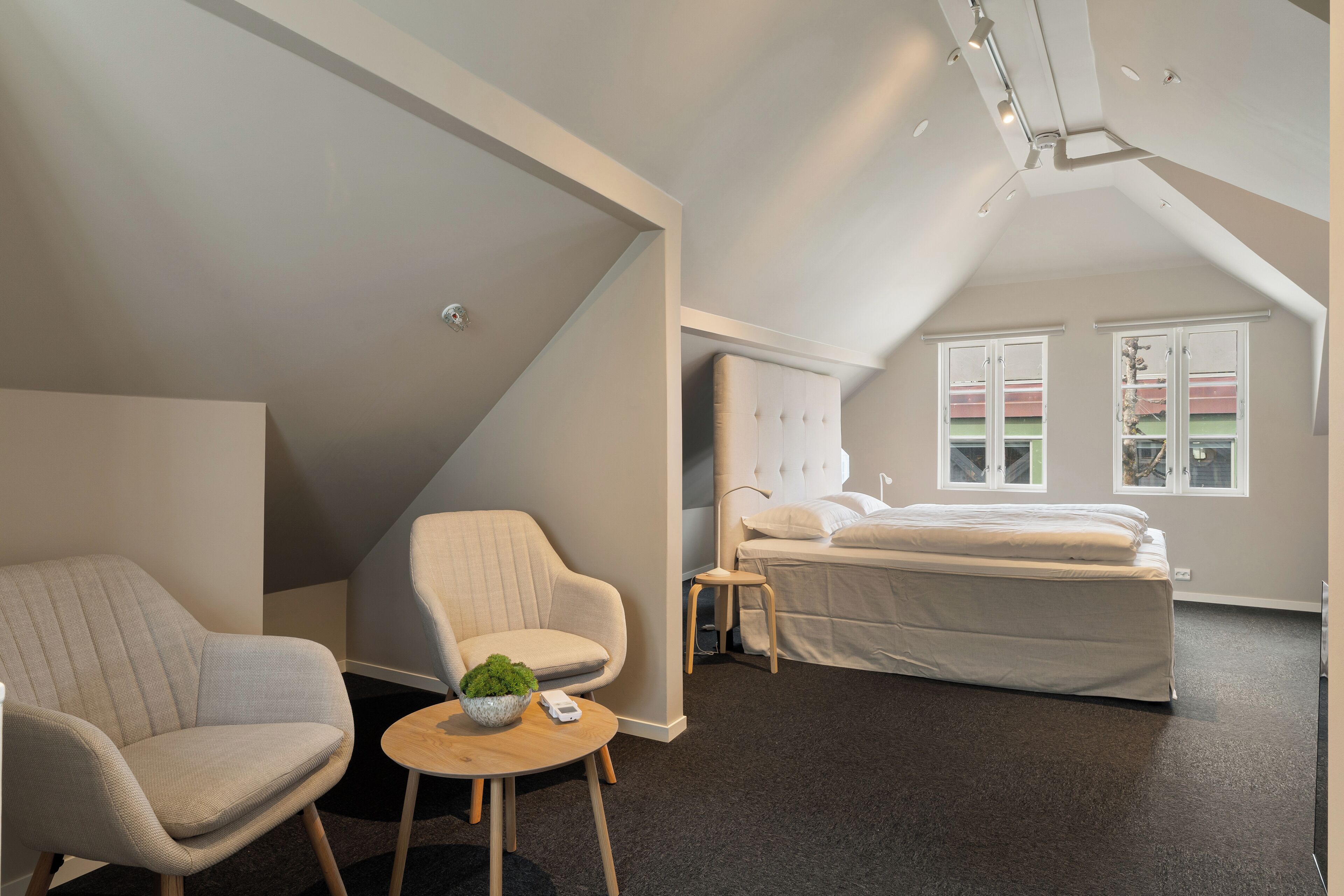A modern bedroom with a loft-style bed, a seating area with a chair and a small table, and a large window providing natural light.