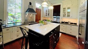 A modern kitchen with a large island, white cabinetry, and stainless steel appliances.