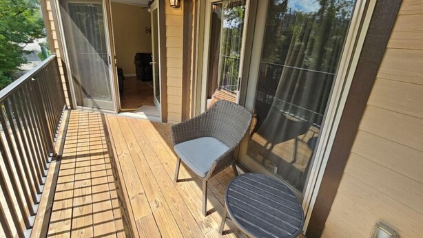A wooden deck with a wicker chair and a small table, a sliding glass door, and a view of the outdoors.
