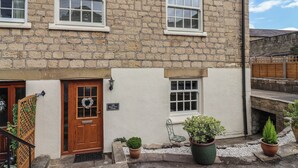Edificio de piedra con puerta de madera, un pequeño porche con plantas en macetas y un letrero que dice "116 Maple Tree Cottage".