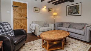 Un salón acogedor con una puerta de madera, dos sofás grises, un sillón de cuero negro, una mesa de centro de madera y una alfombra estampada.