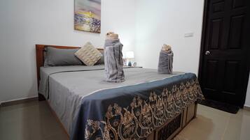 A neatly made bed with a dark blue bedspread and a decorative gold trim, a gray pillow, and two towels draped over the foot of the bed.