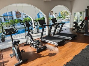 A gym with treadmills, an elliptical, and dumbbells, with a view of a pool and buildings in the background. - Negombo Airport Villa with Pool, Parks and Breakfast (Negombo)