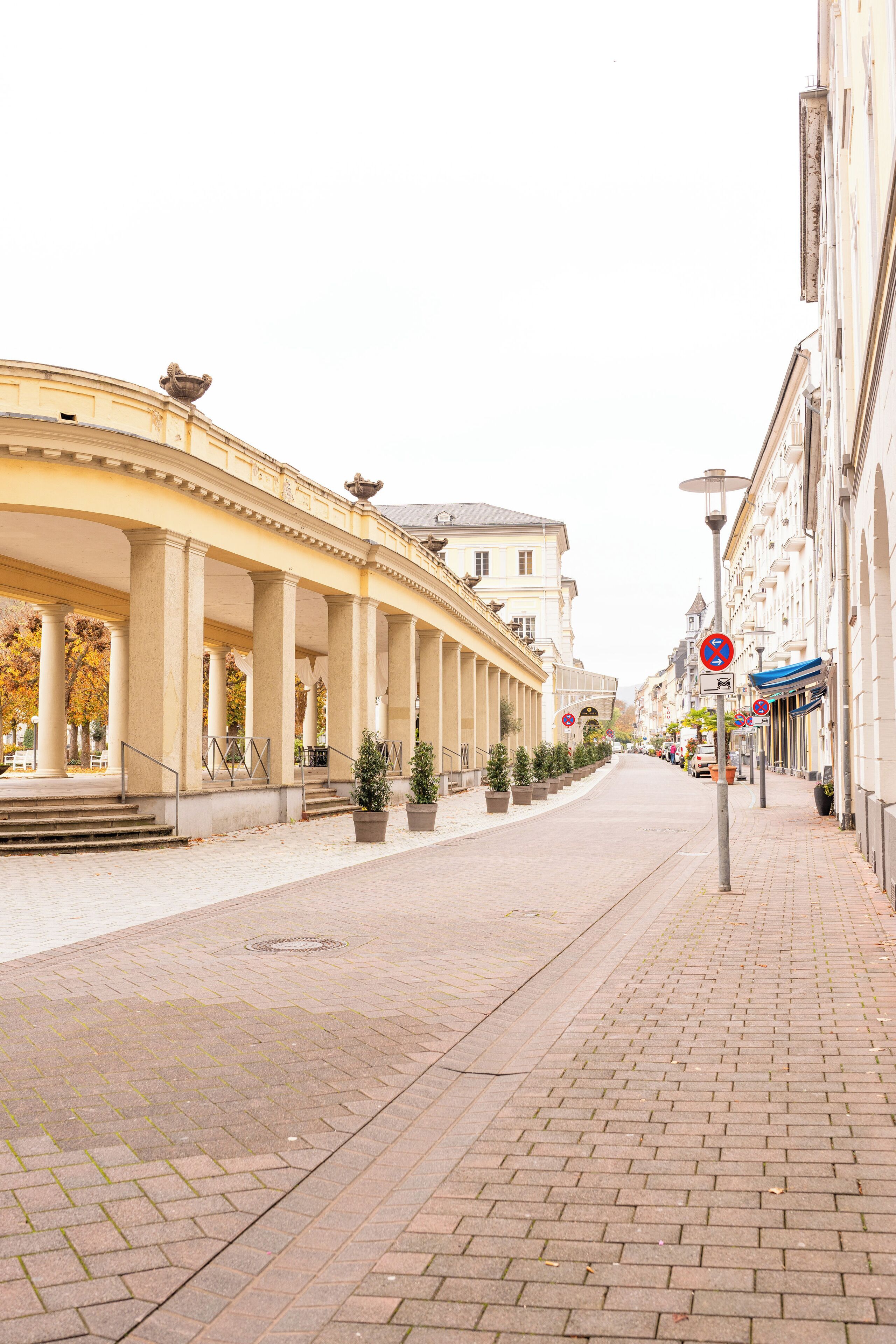 Eine gepflasterte Straße mit überdachter Laube, Blumentöpfen und Gebäuden mit Balkonen.