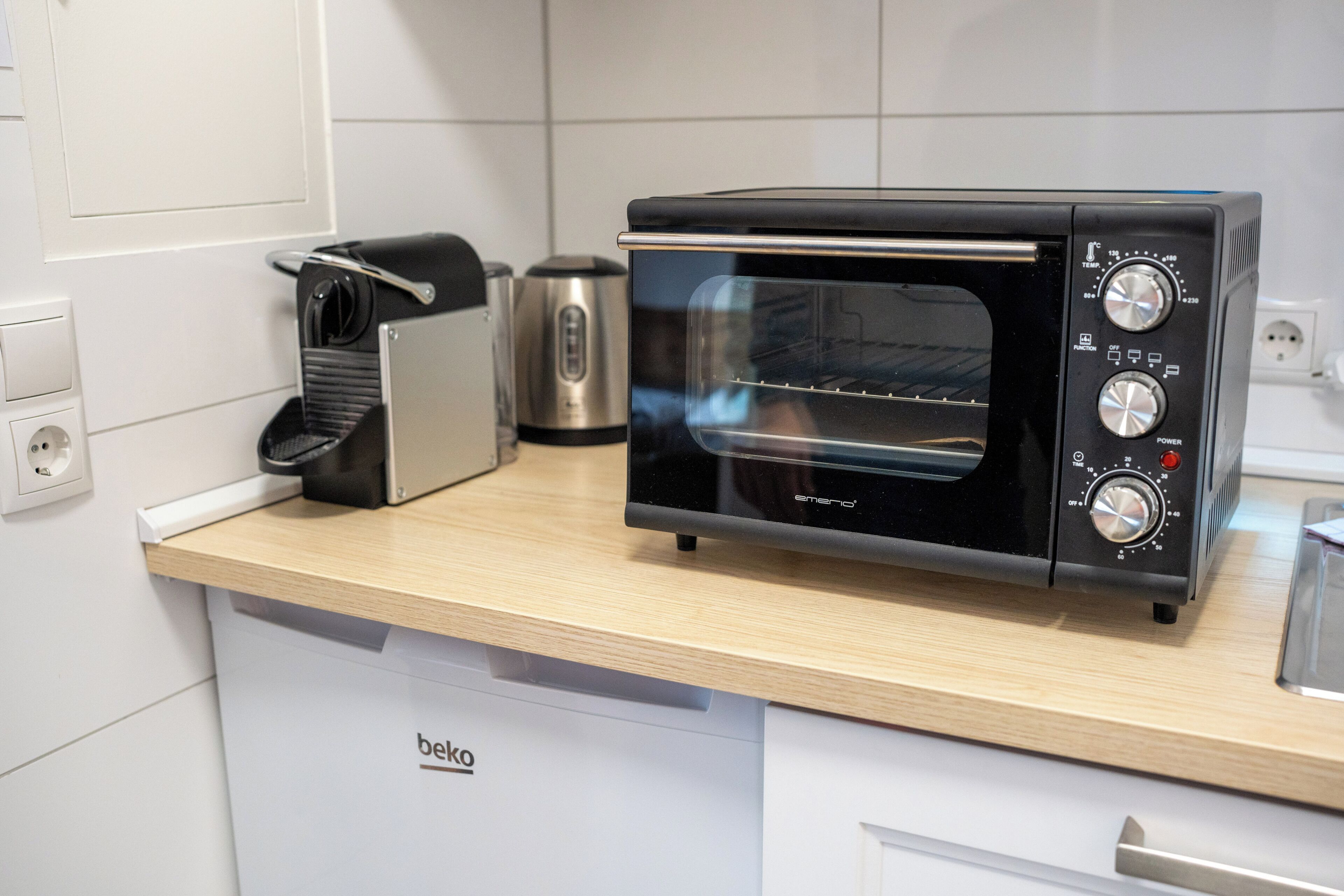 A kitchen with a black toaster oven, a coffee maker, and a kettle on a wooden countertop.