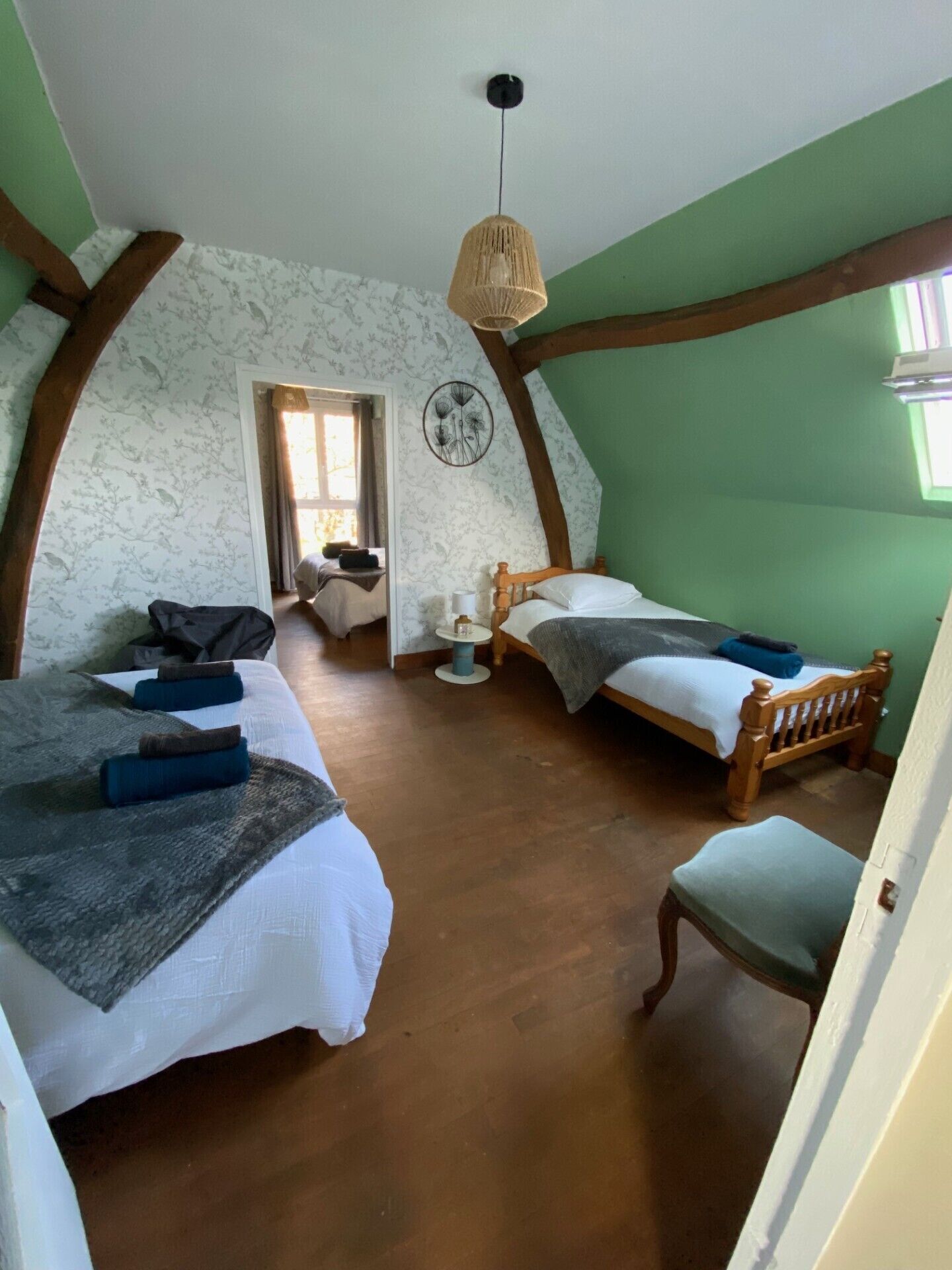 A bedroom with two beds, a wooden chair, a small table, and a hanging light fixture.