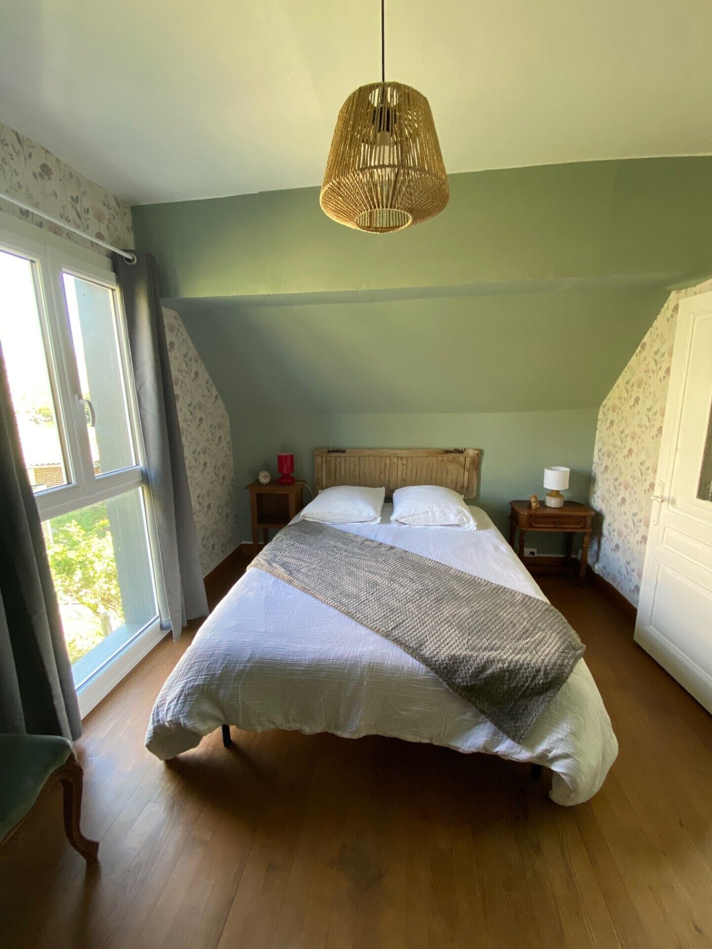 Une chambre à coucher avec un grand lit, un luminaire suspendu, une fenêtre et une porte.