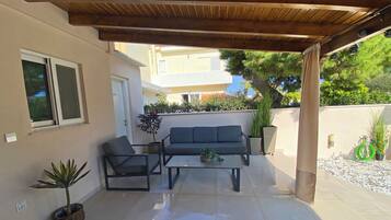 Ein überdachter Patio-Bereich mit einer Couch, zwei Stühlen, einem Couchtisch und Topfpflanzen.