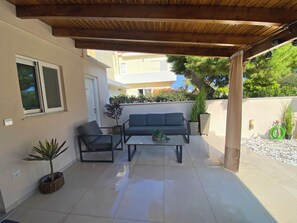 A covered patio area with a sofa, two chairs, a coffee table, and potted plants.