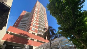 A tall red-brick building with multiple balconies and a covered entrance area.