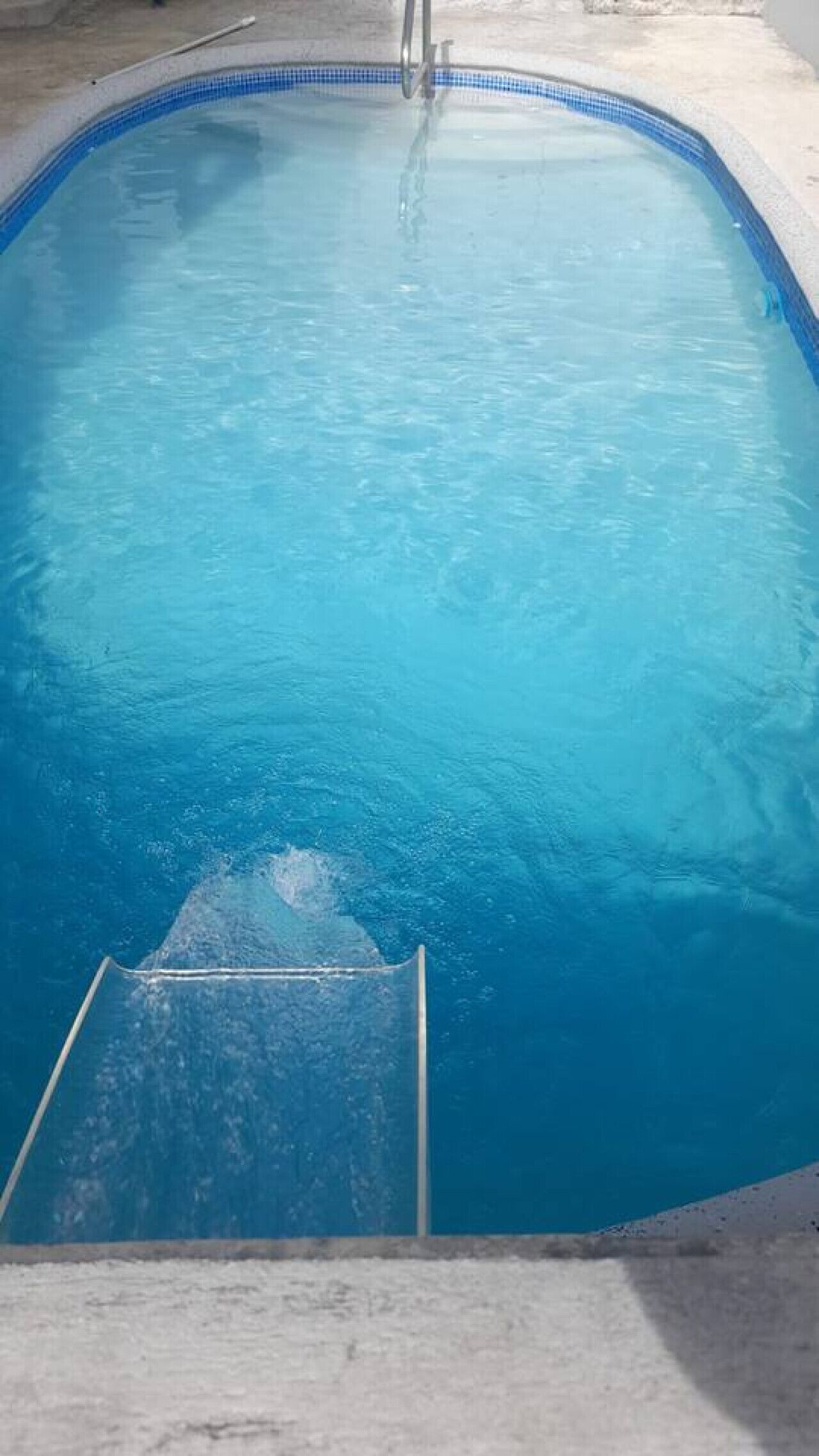 En swimmingpool med krystalklart, blå vand og en metalstige ned til den.