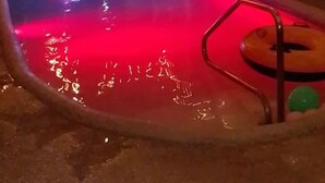 A swimming pool with a red light, surrounded by a covered area with wooden beams and string lights.