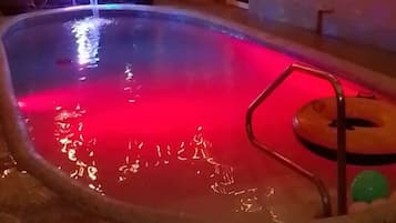 Una piscina con una luz roja, rodeada por un espacio techado con vigas de madera y luces colgantes.