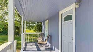 Een overdekte veranda met een balustrade, twee rieten stoelen en een deur.