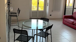 Uma área de refeições com mesa e cadeiras de vidro, um sofá vermelho e uma varanda com vista.