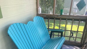 Un banc bleu, doté d’un dossier et d’accoudoirs, est placé sur un sol recouvert d’une moquette bleue, à côté d’une fenêtre donnant sur une pelouse verdoyante.