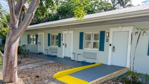 A building with a covered walkway, doors with numbers, and a tree. - ADA Poolside King Studio (Marco Island)