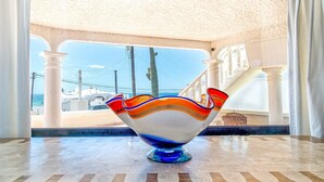 Un bol en verre aux couleurs vives, posé sur un sol de marbre près d’une fenêtre donnant sur une zone côtière.