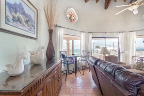 A living room with a leather sofa, a dining table with chairs, a vase with dried plants, and a framed picture on the wall. - Casa Tres Amigas Cozy Ocean View Retreat Las Conchas (Puerto Peñasco)