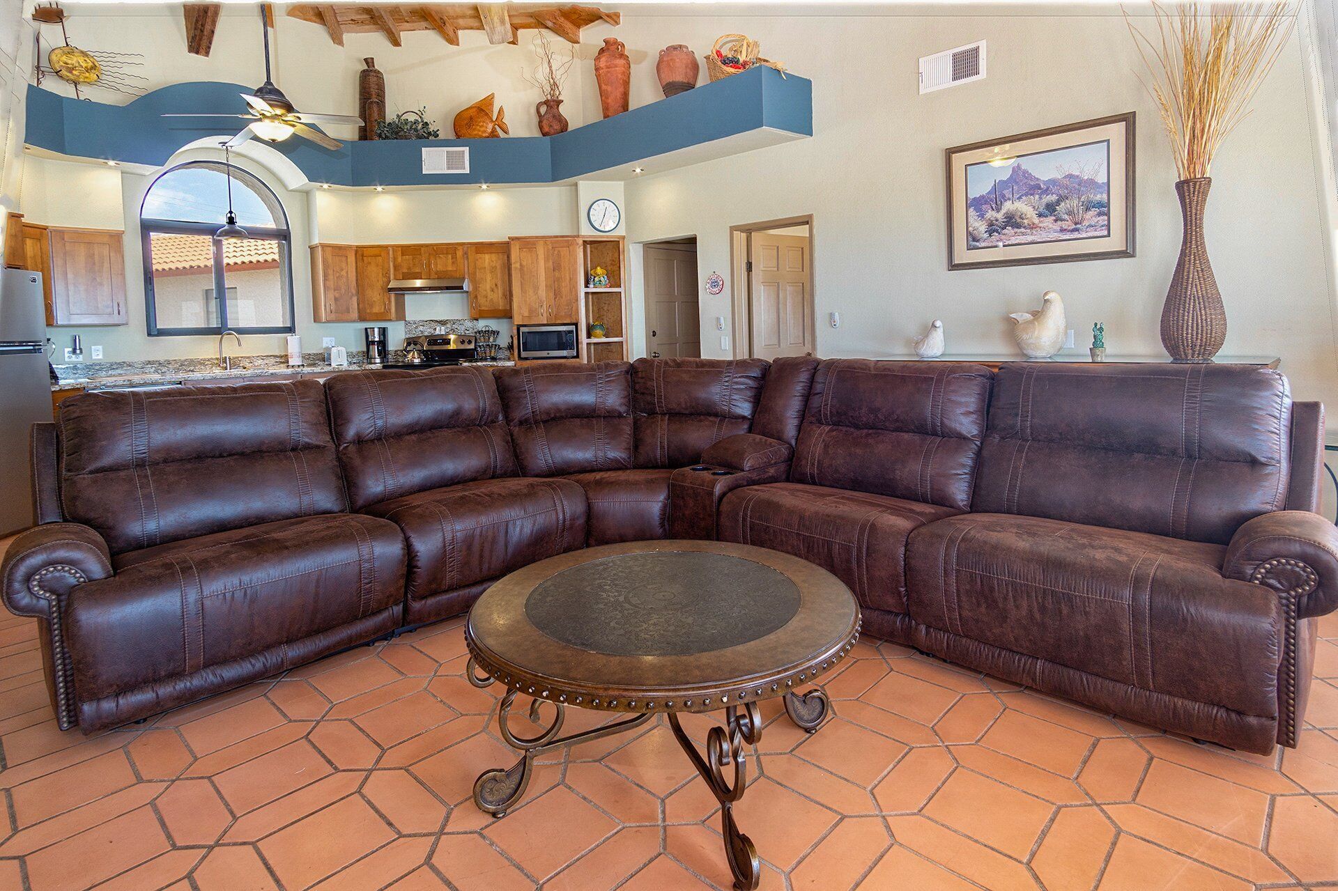 A spacious living room with a large brown leather sectional sofa and a round metal coffee table.
