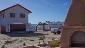 A white building with a red roof, a garage, and a sandy beach in the foreground. - Casa Azalea -brand New- Modern Beachfront Home Playa Encanto (Puerto Peñasco)