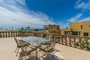 Une terrasse avec une table et des chaises en verre, donnant sur une plage et un ciel bleu azur.