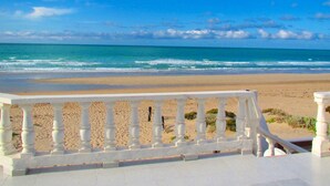 Een strand met een witte balustrade op de voorgrond en een helderblauwe lucht.