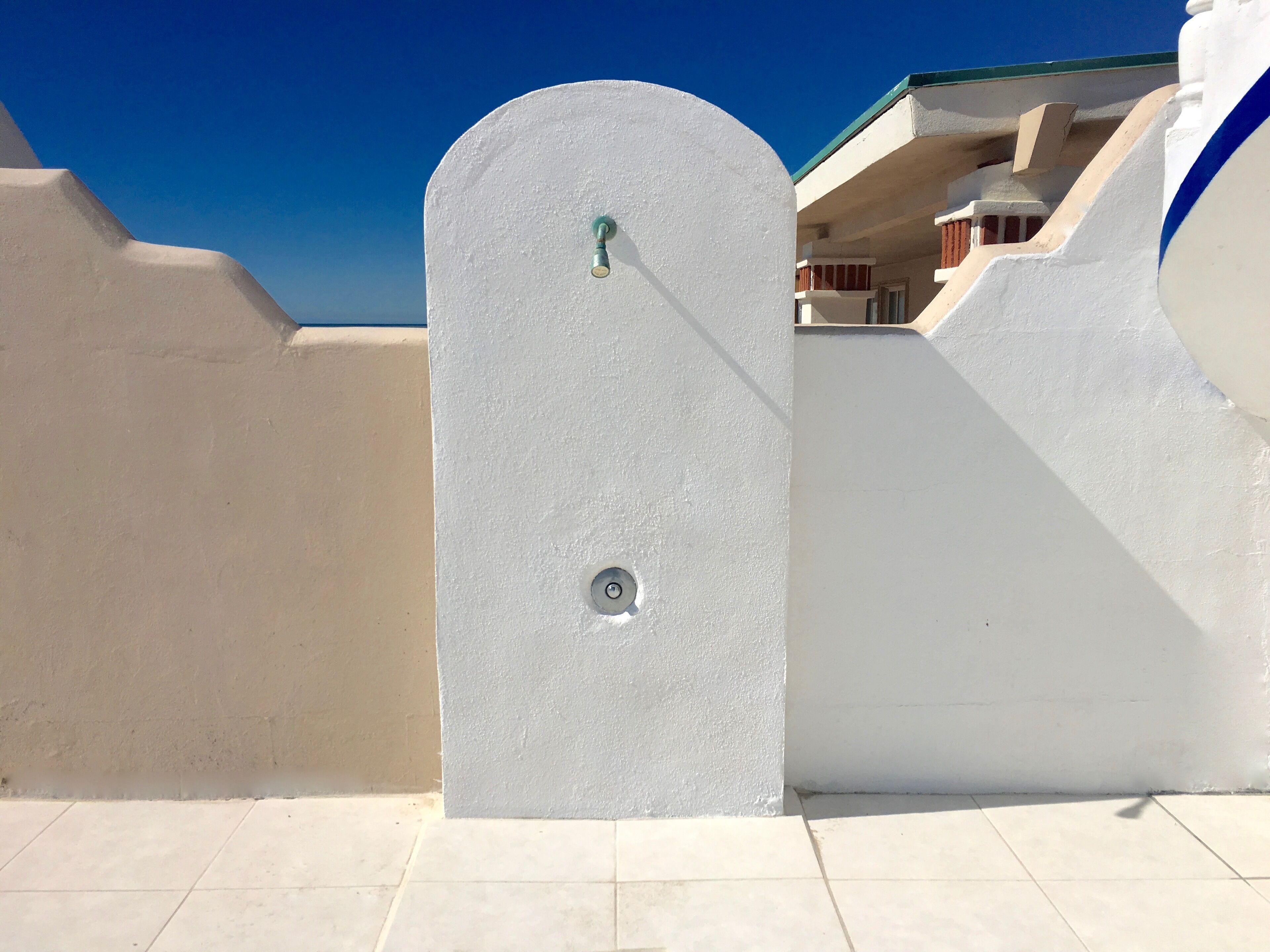 Una puerta arqueada blanca con un pomo de metal, que da paso a un edificio de fachada blanca y detalles azules.