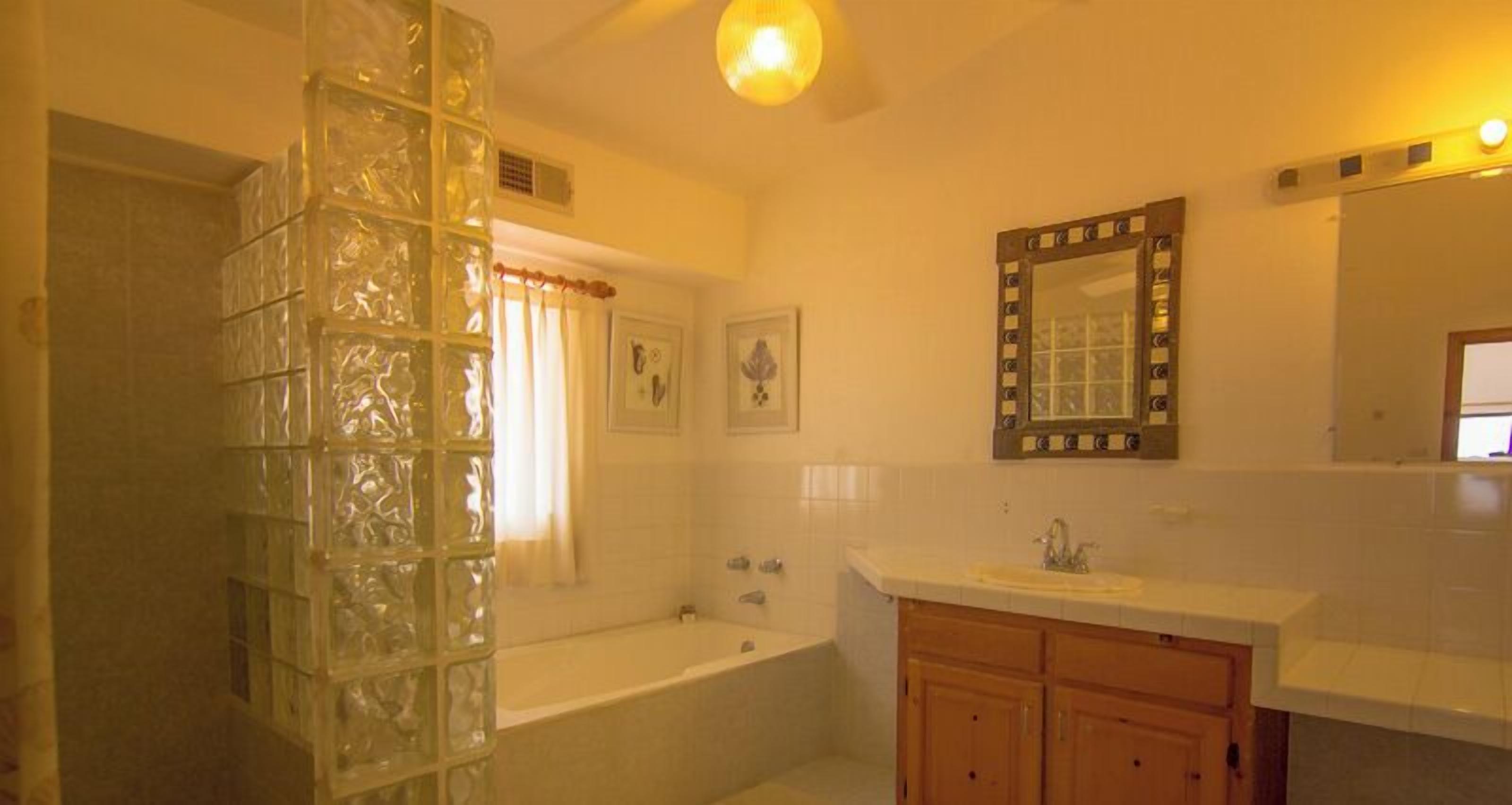 A bathroom with a glass shower enclosure, a bathtub, a sink with wooden cabinets, and a mirror with a decorative frame.