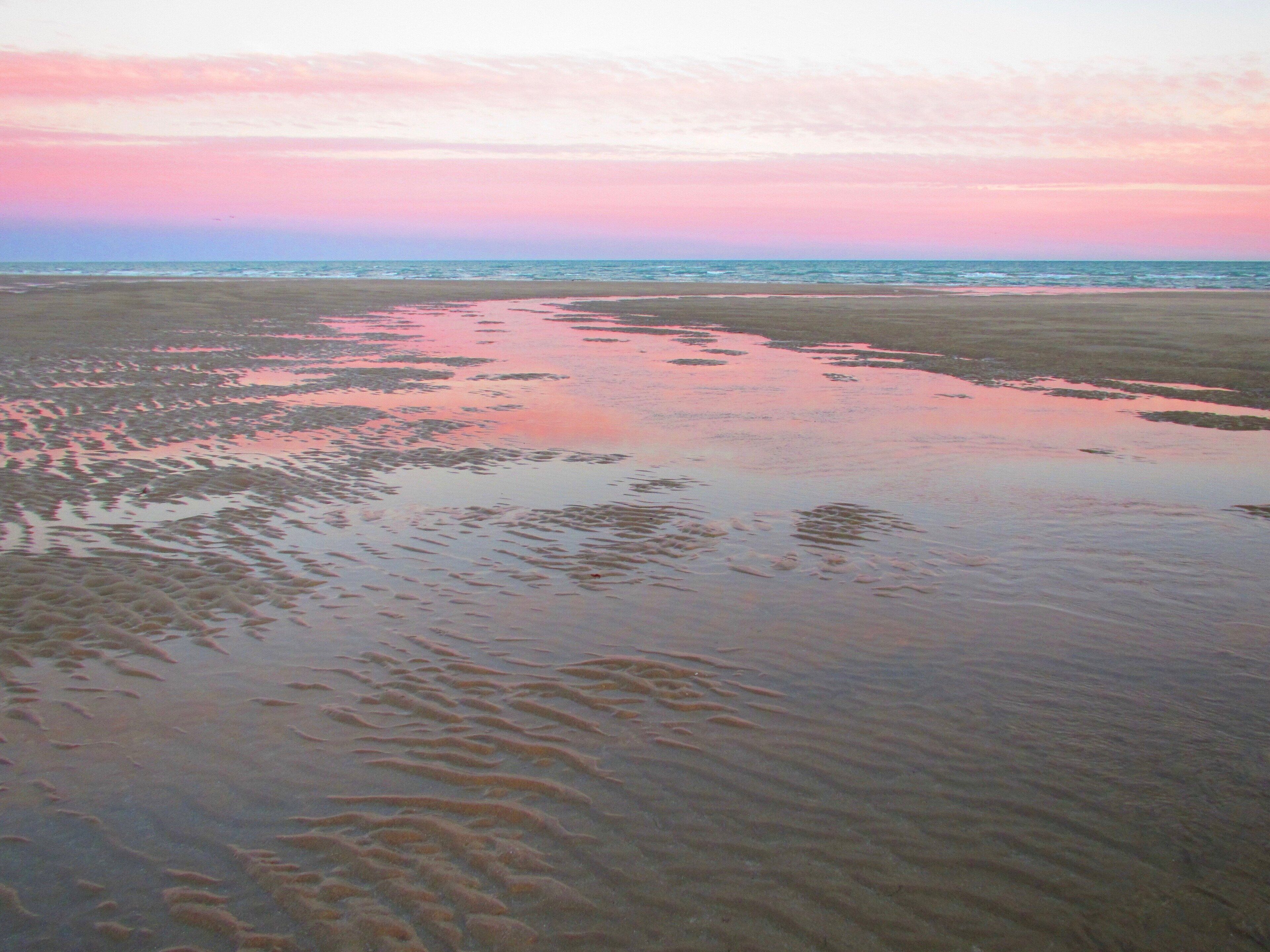 Ein Strand mit feuchtem Sand und sanften Wellen.