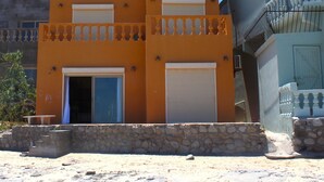 A two-story building with a stone foundation, a balcony with balustrades, and two garage doors. - Casa Arco Iris Brand New 2-story Spacious Home Cholla Bay Ocean Front (Puerto Peñasco)