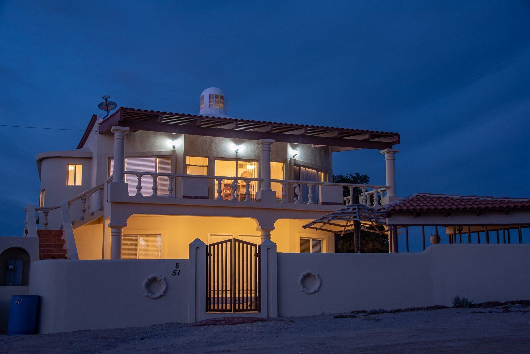 Una casa de dos pisos con balcón, antena parabólica y entrada protegida por una reja.