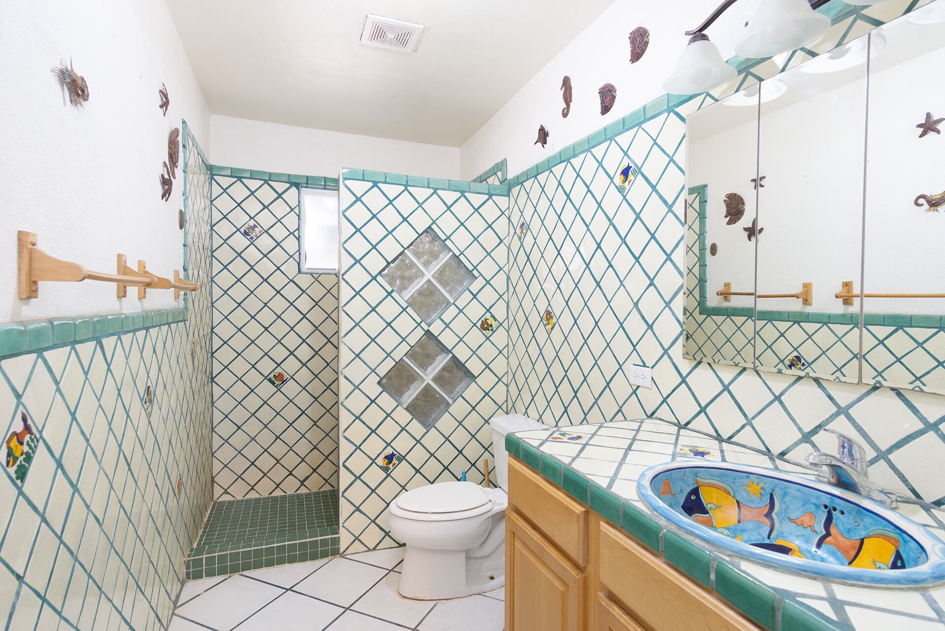 Une salle de bain avec un sol carrelé, des toilettes, un lavabo au design coloré et un espace douche doté d’une porte en verre.