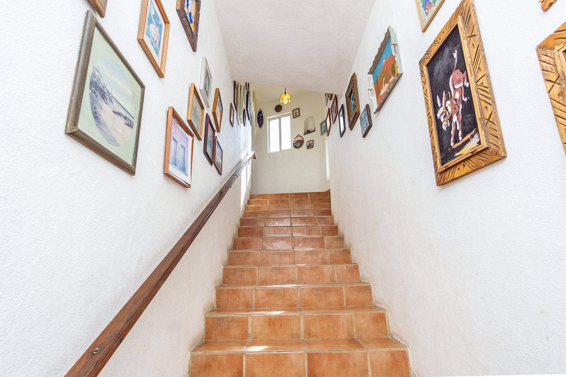Un escalier avec une rampe en bois mène à un palier où se trouve une porte. Les murs sont ornés de nombreuses images encadrées.