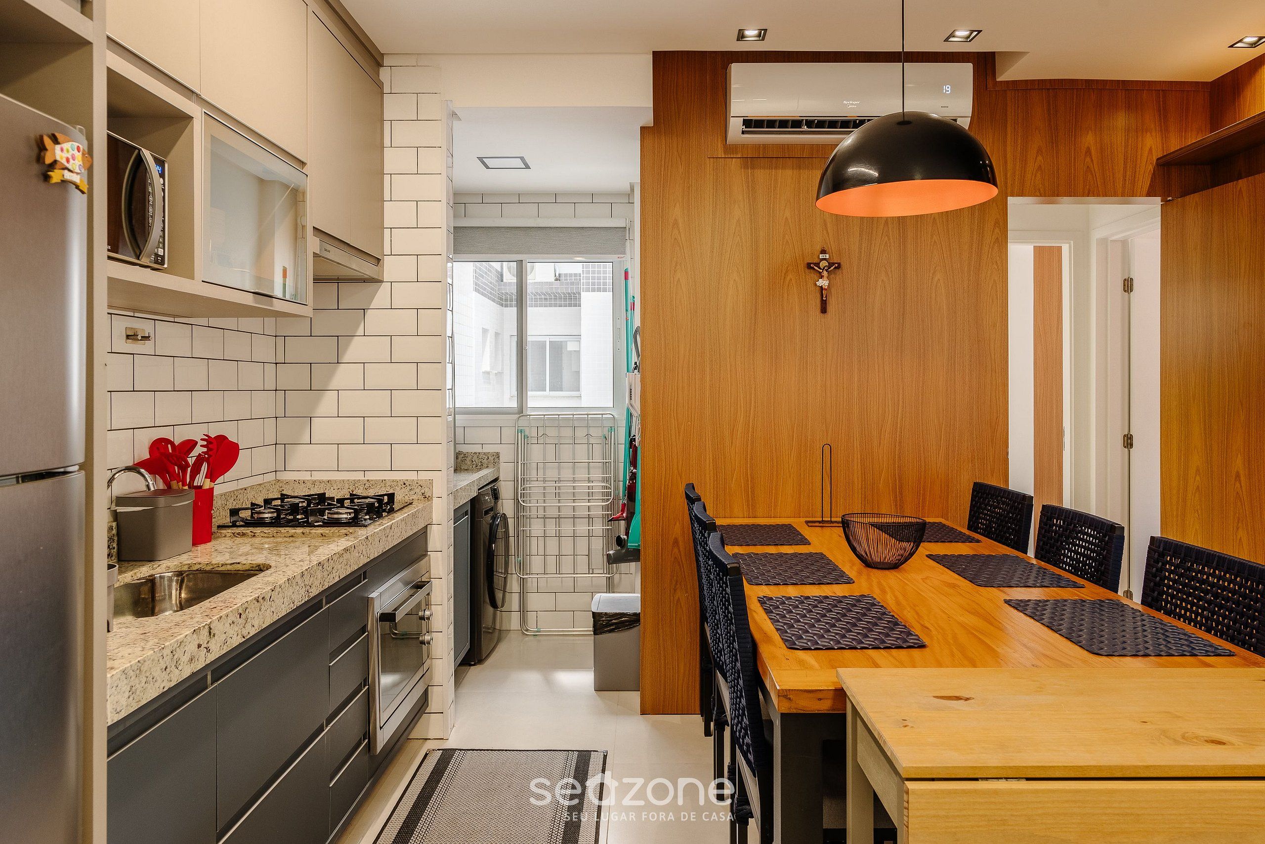A modern kitchen with a dining area, featuring a wooden dining table, black chairs, and a pendant light.