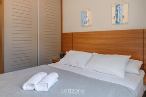 A neatly made bed with white linens and two pillows, a wooden headboard, and a small bedside table with a plant. - Cozy Apartment w Barbecue 550m - Beach Ire021 (Ubatuba)