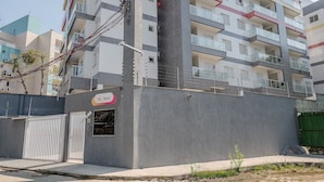 Un edificio residencial de varios pisos con balcones, una entrada con portón y un letrero que indica un negocio o servicio en la planta baja.