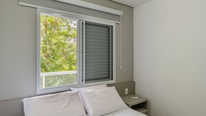 Un dormitorio con cama, mesita de noche y ventana con persianas.