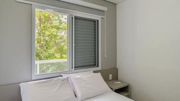 Un dormitorio con cama, mesita de noche y ventana con persianas.