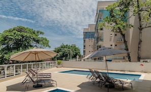 A rooftop pool area with lounge chairs and umbrellas, surrounded by a high-rise building. - Comfort and Leisure 500m From the Beach - Ire0022 (Ubatuba)