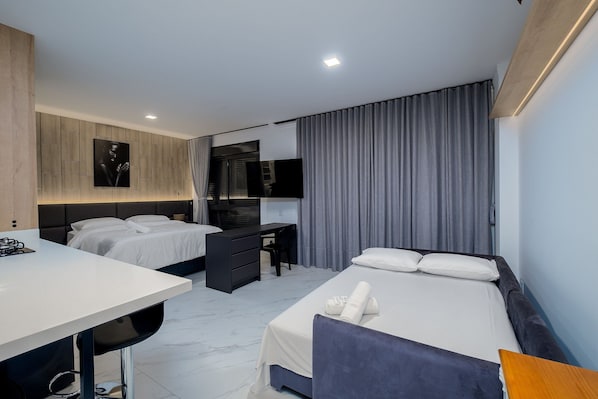 Ein modernes Hotelzimmer mit einem Bett, einem Schreibtisch, einem Sessel, einem kleinen Tisch und einem Fernseher.