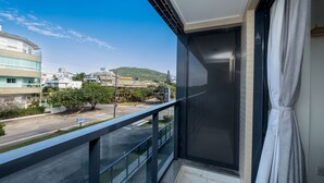 A balcony with a view of a road and buildings, a glass door, and a curtain. - High Standard Studio on the Sand in Floripa Irb205 (Florianópolis)