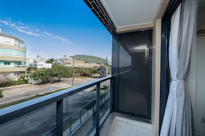 Ein Balkon mit Blick auf eine Straße und Gebäude, eine Glastür und ein Vorhang.