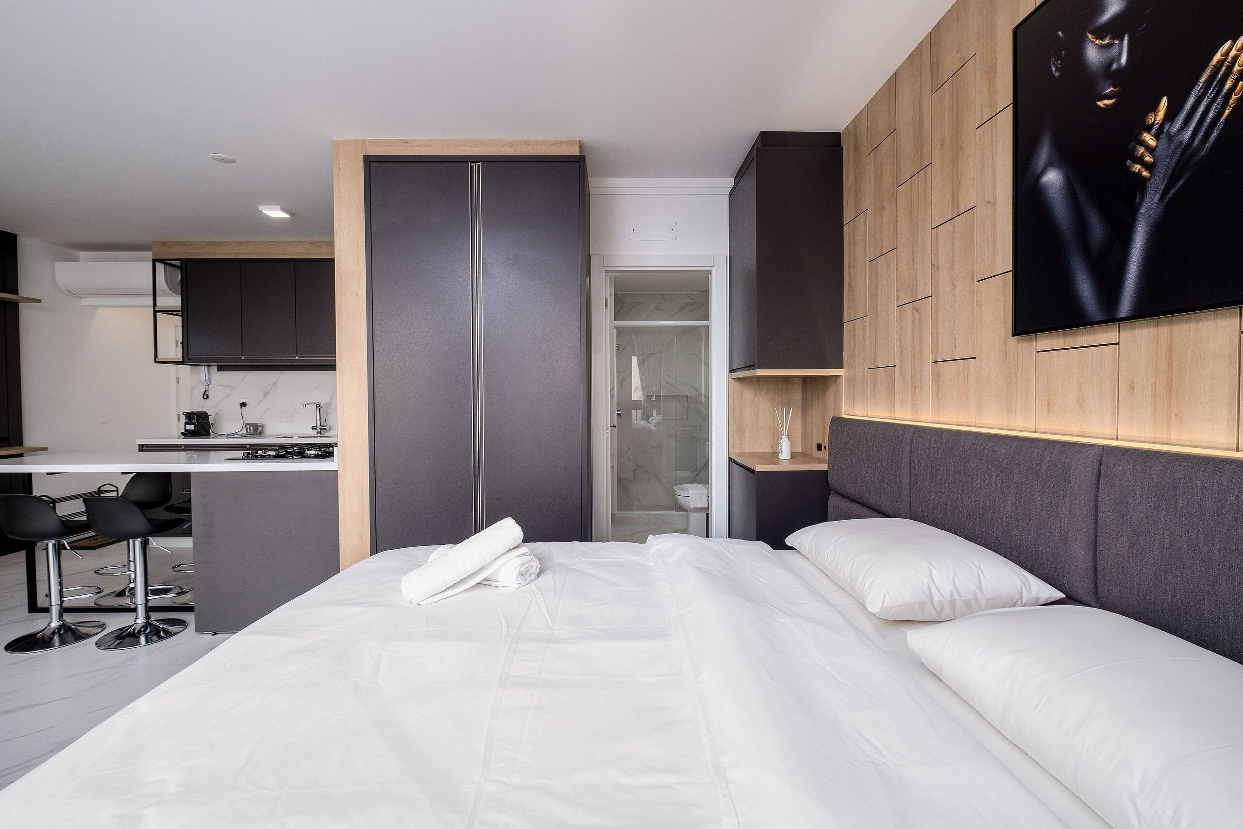 A modern hotel room with a bed, a desk, and a kitchenette.
