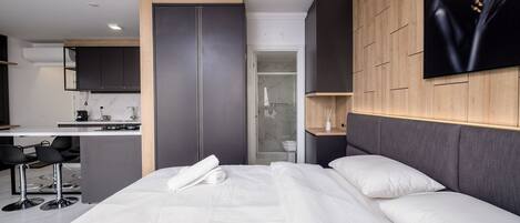 A modern hotel room with a bed, a desk, and a kitchenette.