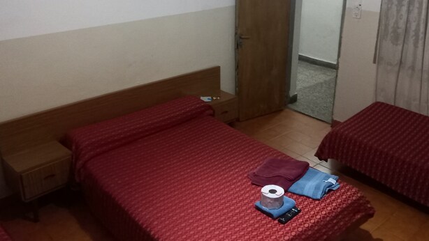 A bedroom with a single bed, a wooden wardrobe, a small bedside table, and a door leading to another room. - Hotel Florentino (Buenos Aires)