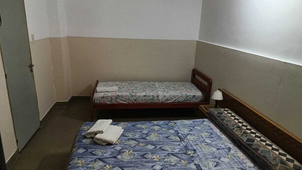A small, compact room with two single beds, each with a different patterned bedspread. There is a small table with a lamp next to one bed. - Hotel Florentino (Buenos Aires)
