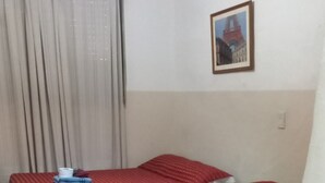 A room with two beds, a checkered floor, a curtain, a framed picture, and a lamp. - Hotel Florentino (Buenos Aires)