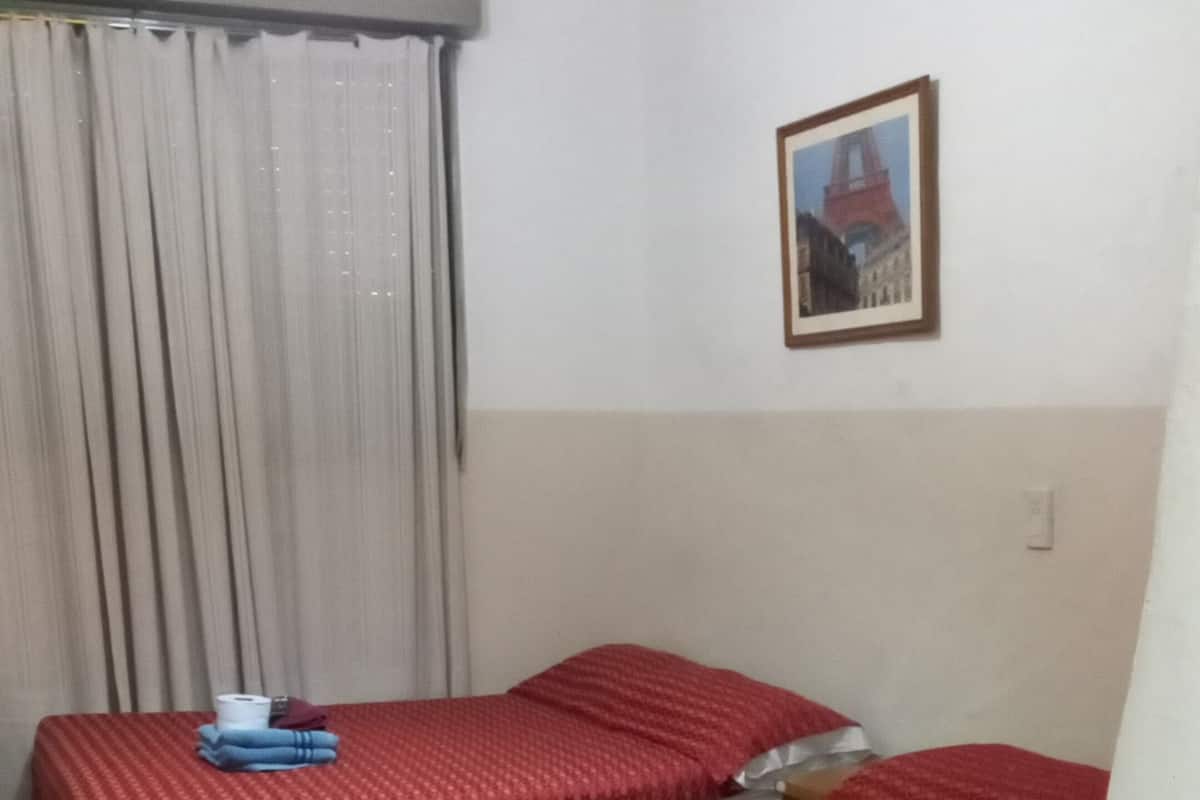 A room with two beds, a checkered floor, a curtain, a framed picture, and a lamp.